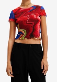 Lyhytnhihainen punainen crop-top, jossa on pyörivä abstrakti kuosisininen, vihreä ja keltainen korostus; röyhelöhelma.