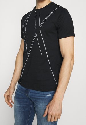 Schwarzes Baumwoll-T-Shirt mit weißen Buchstaben in diagonalen Linien, Rundhalsausschnitt und kurzen Ärmeln. Getragen mit blauen Jeans.