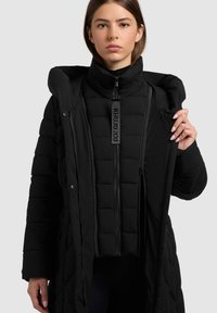 Zwarte pufferjas met een hoge kraag, ritssluiting aan de voorkant en drukknoopsluitingen. De binnenkant heeft een afneembare geïsoleerde laag.