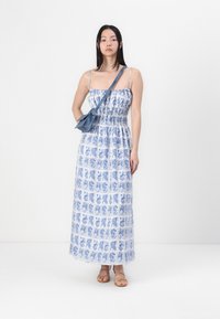 Abito lungo con un motivo a piastrelle bianche e blu, caratterizzato da un corpetto smock e spalline sottili. Abbinato a una borsa a tracolla blu e sandali.