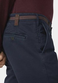 Marineblaue Herrenhosenträger mit einem braun gemusterten Bund, Knopfverschluss, seitlichen Taschen und dezentem Branding auf der Gesäßtasche.