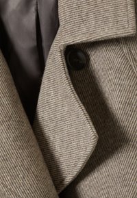 Bruine gestreepte wollen jas met een pieklapel en een zwarte knoop, met een gladde grijze voering zichtbaar onder de kraag.