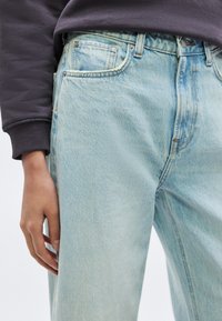 Svetlo modri kavbojki iz jeansa z visokim pasom, sproščenim krojem in nežnim bledenjem. Ima sprednje žepe in okrepljene šive.