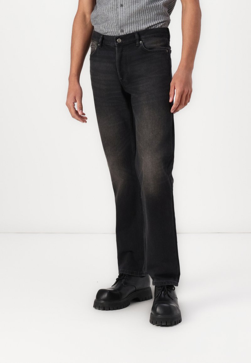 Jeans negri din denim cu un design drept, textură decolorată, buzunare frontale și închidere cu buton, asortați cu pantofi negri cu șiret.