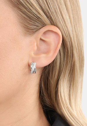 Los pendientes de aro de plata presentan un diseño entrelazado con una superficie texturada y acentos claros y brillantes, mostrando un acabado metálico pulido.