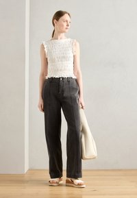 White smocked top with ruffled edges, paired with high-waisted, wide-leg dark gray jeans and beige platform sandals. Accessorized with a cream bag.