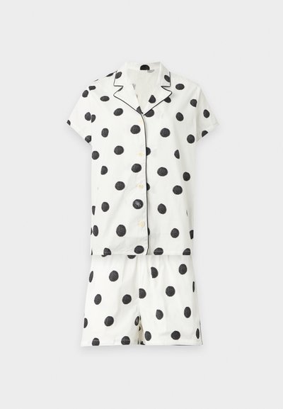 Chemise blanche à manches courtes boutonnée et short assorti avec de gros pois noirs et passepoil noir sur le col et les bords.
