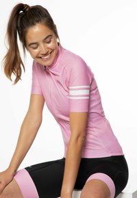 Ružový cyklistický dres s krátkymi rukávmi a vysokým golierom, s bielymi pruhmi na rukáve. Nosený s čiernymi cyklistickými šortkami.