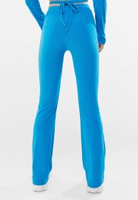 Blue cotton blend flared pants with a drawstring waist. Soft texture and embroidered detailing on the back. Finished with white footwear.