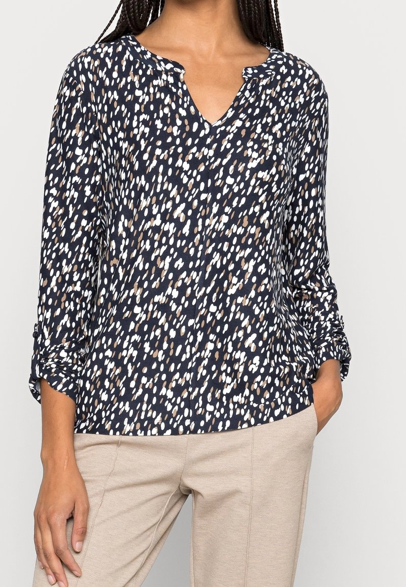 Navybluse mit einem weiß-braun gesprenkelten Muster. Sie verfügt über einen V-Ausschnitt, lange Ärmel mit umgeschlagenen Manschetten und einen weichen, strukturierten Stoff.