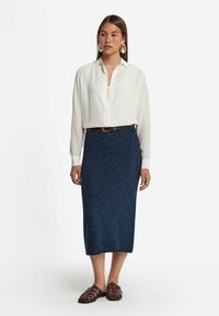 Vit skjorta med lång ärm och knappar, som kombineras med en knälång, mörkblå texturerad kjol, accentuerad med ett brunt bälte och bruna sandaler.