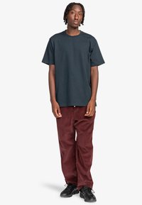 Mørkeblå bomuld T-shirt, parret med burgunder kordfløjlsbukser. Har en afslappet pasform og diskret branding på brystet. Sorte sneakers fuldender looket.