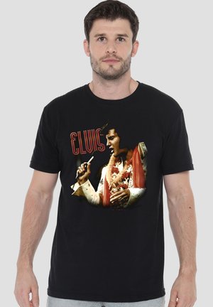Mann trägt schwarzes T-Shirt mit buntem Bild von Elvis Presley, der in ein Mikrofon singt, und dem Schriftzug "ELVIS" darüber.