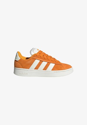 Zapatilla Adidas de ante naranja con rayas blancas, suela blanca y cordones, vista desde el lado externo sobre un fondo blanco.