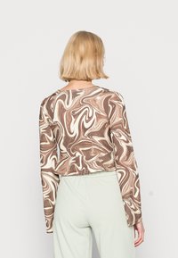 Top de manga longa com um padrão de mármore em tons de castanho e creme; tecido leve com gola redonda e barra cropped. Combinado com calças verde menta.