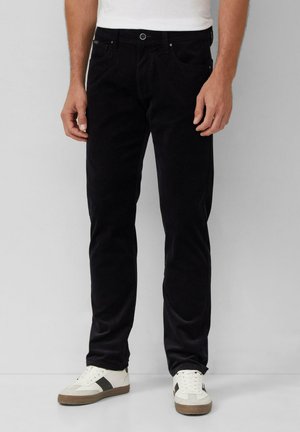 Schwarze Cord-Hosen mit geradem Schnitt, Fünf-Taschen-Design und sichtbaren Nähten, kombiniert mit weißen Sneakers mit dunklen Akzenten.