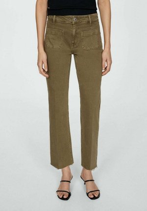 Olivengroene rechte broek met voorzakken en onafgewerkte zoom, gedragen met zwarte sandaalhakken met open tenen en een zwart topje.