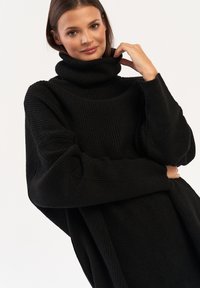 Czarny sweter z golfem, wykonany z prążkowanej dzianiny; charakteryzuje się oversize'owymi rękawami i luźnym krojem. Minimalistyczny design bez dodatkowych wzorów.