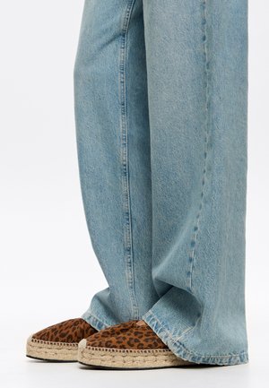 Espadrillas con un design a stampa leopardata, marroni e beige, con una suola in juta intrecciata. I pantaloni in denim azzurro coprono parzialmente le scarpe.
