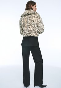 Jakke i kunstpels i cremefarve med sorte pletter, med bred krave, kort design, og stylet med tætsiddende sorte bukser og høje hæle.