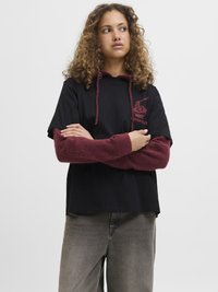 Hoodie noir à manches courtes avec une manche en fausse fourrure bordeaux, comportant un design graphique sur la poitrine et une capuche avec cordon de serrage. Assorti à un jean gris.