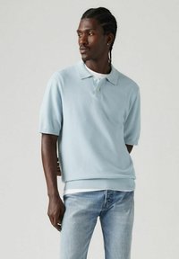 Vaaleansininen lyhythihainen polo-paita pehmeästä neulomateriaalista, jossa on käännettävä kaulus sekä hillityt ribbipäärmeet hihansuissa ja helmassa.