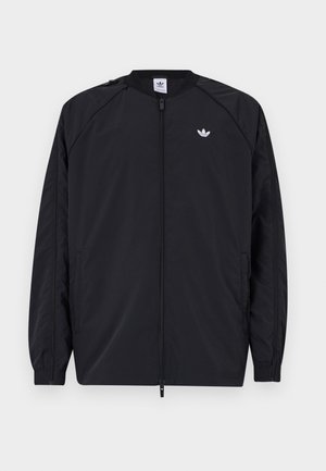 Must 黑色轻便夹克,带拉链前襟,弹性袖口,左胸有一个小白色标志。特点是简单、干净的设计。