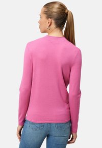 Měkký růžový svetřík s dlouhým rukávem, žebrovaným límcem a přiléhavým střihem, s viditelnými detaily švů, nošený s modrými džínami.