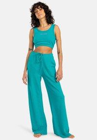 Teal crop top tank met logo-tekst aan de voorkant en bijpassende losse sweatpants met koord in de taille. Zachtheid en comfortabel ontwerp.