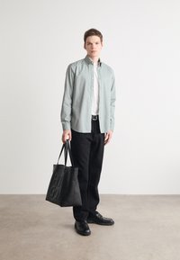 Lichtgroen knopshirt, wit T-shirt eronder, zwarte loszittende broek, zwarte leren schoenen en een gestructureerde zwarte tote bag.
