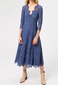 Vestido de encaje en azul marino con escote en V, mangas de tres cuartos y falda acampanada. Presenta intrincados patrones florales y un dobladillo con puntas.