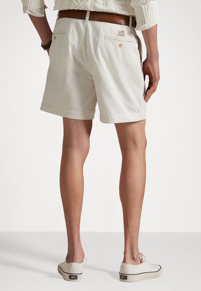 Beige cotton shorts with a straight cut and back pockets, paired with light-colored shoes, worn with a cream sweater.