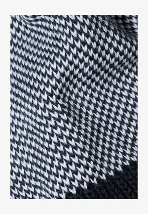 Strickstoff mit einem schwarz-weißen Zickzack-Muster, das sichtbare Textur und Fasern aufweist und ein weiches, gewebtes Design zeigt.