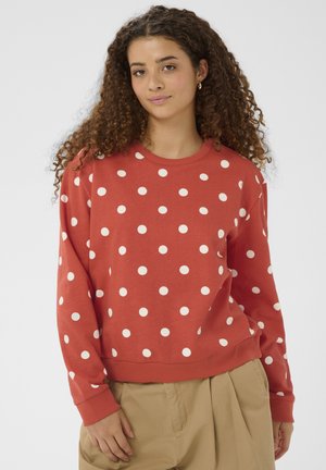 Felpa rossa con pois bianchi, scollo rotondo e polsini a costine. Tessuto morbido con vestibilità comoda, abbinata a pantaloni chiari.