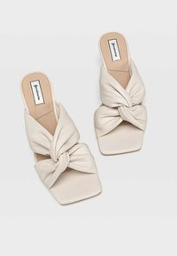 Mules beiges à bout carré avec un supérieur en satin noué et une semelle lisse et plate. Design minimaliste avec une texture lisse.