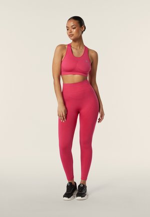 Reggiseno sportivo rosa e leggings all'altezza della vita abbinati, realizzati in tessuto elasticizzato, con orli a costine e una texture liscia. Scarpe sportive nere.