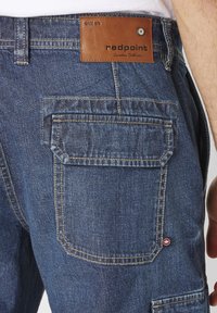 Blue denim shorts featuring a brown leather patch with "redpoint" text, double back pockets, and contrasting yellow stitching.