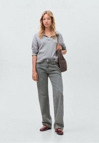 Grijze gebreide trui met V-hals, gecombineerd met hooggesneden, loszittende grijze denim jeans. Bruine tas met een hengsel, bordeauxrode loafers.