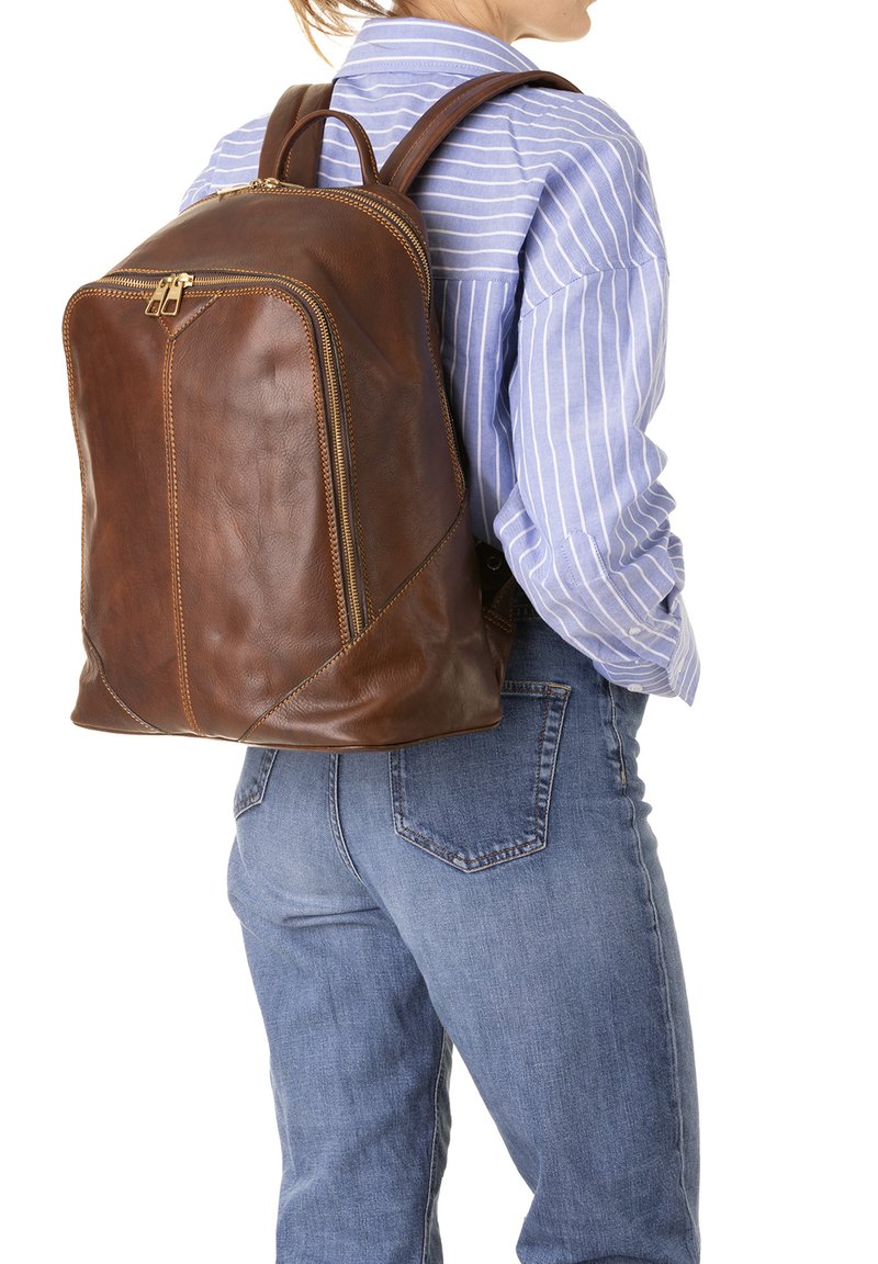 Sac à dos en cuir brun avec une texture lisse, double fermeture éclair et coutures accentuées. Les bretelles réglables et un design épuré sont visibles.