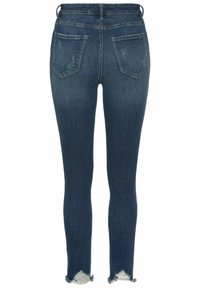 Chudé tmavo modré rifle s výraznými zadnými vreckami a rozstrapkanými okrajmi. Vyrobené z denimovej tkaniny s miernym vyblednutím. Žiadne viditeľné kovové súčasti ani ozdoby.