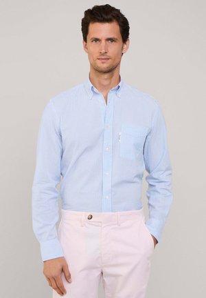 Camisa de botones de rayas azul claro y blanca, hecha de una tela ligera, que presenta un bolsillo en el pecho y puños con botón, combinada con pantalones rosa pálido.