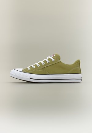 Zapatilla baja de lona en verde oliva con cordones blancos, puntera de goma y suela blanca con franjas negras.