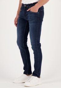 Slim-fit, dark blue denim jeans with five pockets, slight fading, and a button front. Paired with white sneakers.
