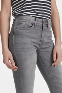 Jeans grises de tiro alto con una textura suave, cinco bolsillos y accesorios en tono cobre. Diseñados para un ajuste slim, se presentan con una camisa a rayas.