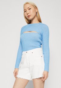 Top de manga larga de canalé azul cielo con un diseño recortado, combinado con pantalones cortos blancos de cintura alta con dobladillo deshilachado y cierre de botón.