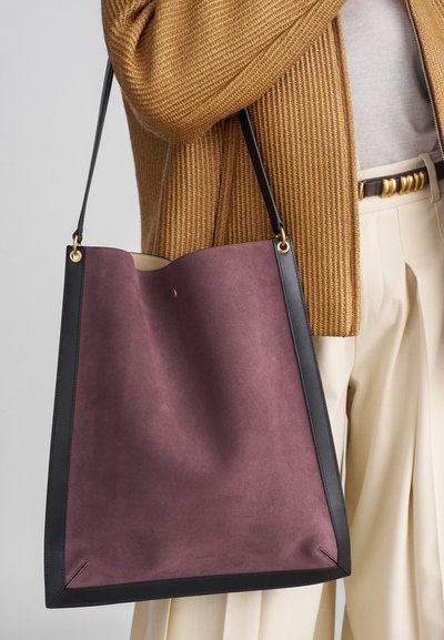 Grote tote bag van donkerpaarse suede met zwarte leren randen en gouden hardware. Gladde textuur met een open bovenkant en minimale stikdetails.