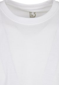 Biela bavlnená tričko s okrúhlym výstrihom. Obsahuje jemný logotyp v sivej farbe na vnútornom okraji goliera. Hladká textúra, základný dizajn.