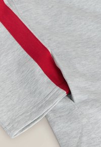 Siva tkanina z gladko teksturo ima rdečo poudarjeno črto ob šivu, ki prikazuje sproščen dizajn in čiste robove.