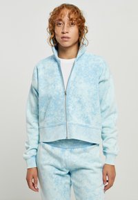 Lyseblå hettegenser med glidelås, med et teksturert sky-mønster, ribbede mansjetter og en kortere design, sammen med matchende bukser. Mykt stoff.