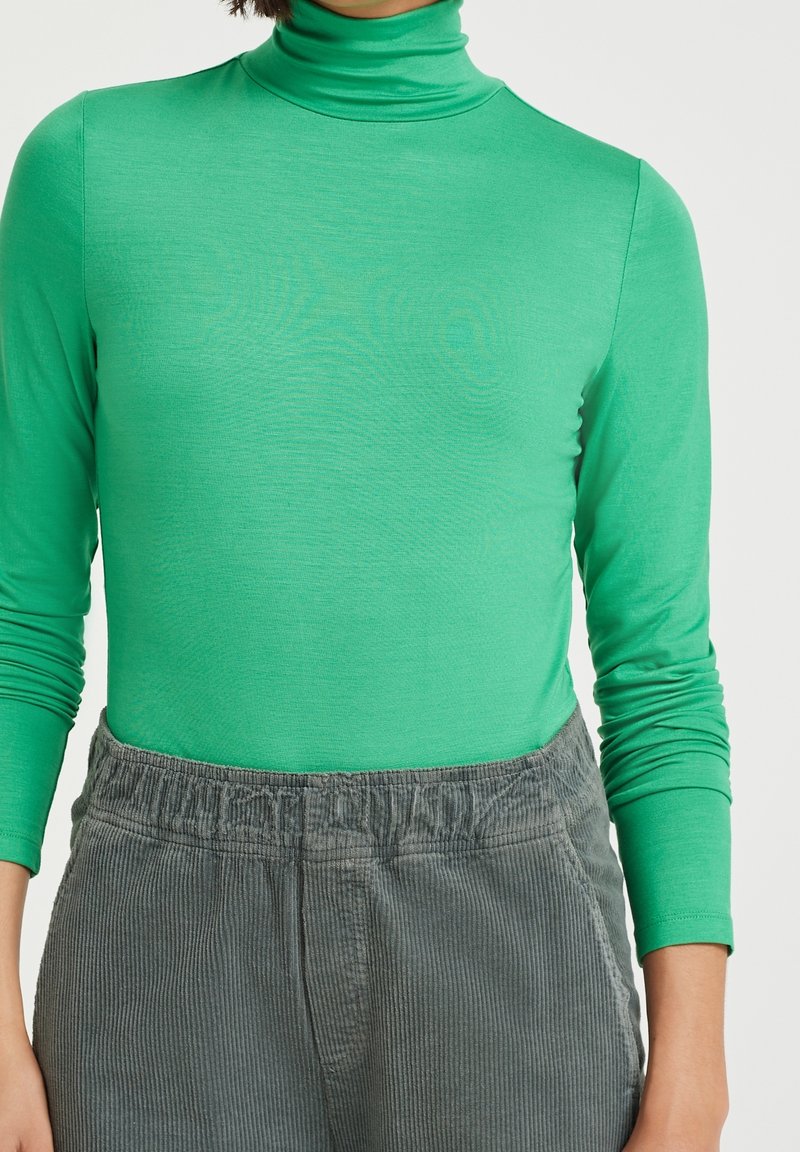 Grön långärmad polotröja i ett glatt, stretcht tyg, kombinerad med grå manchesterbyxor med elastisk midja och vertikala ränder.